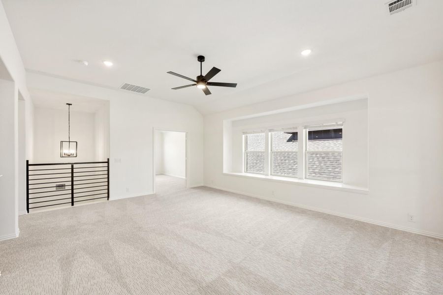 Spacious upstairs loft with carpet, ceiling fan, black metal railing, and large windows