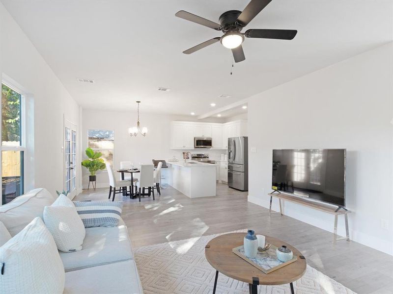 Living room featuring light wood-type flooring and ceiling fan with notable chandelier