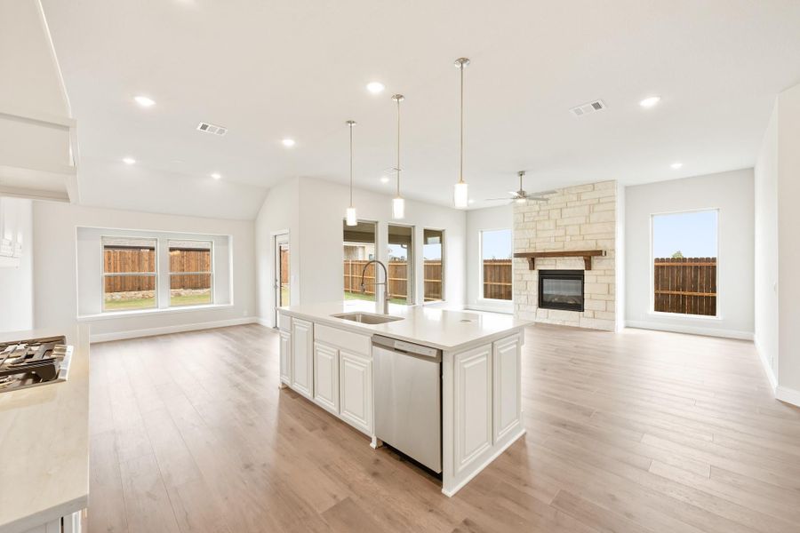 Open-concept kitchen and living area with white island, stone fireplace, and hardwood floors