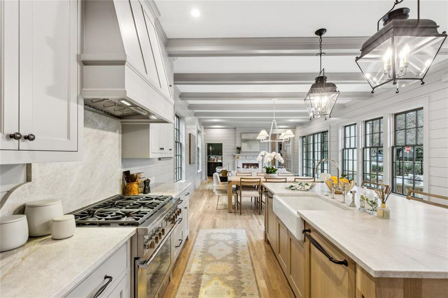 Kitchen with white cabinets, light stone counters, hanging light fixtures, stainless steel appliances, and a sink