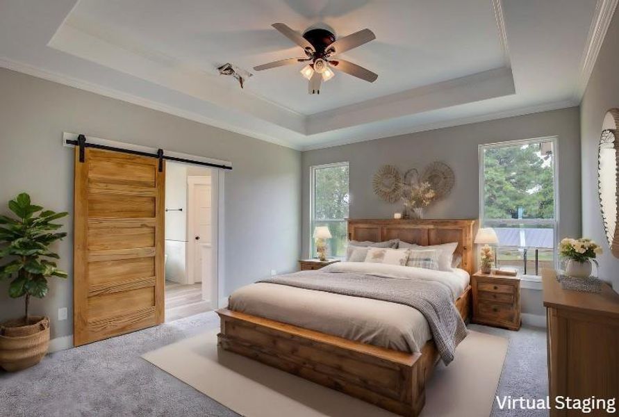 Carpeted bedroom with ceiling fan, ornamental molding, a barn door, and a tray ceiling