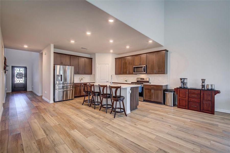 Kitchen with a breakfast bar, stainless steel appliances, light hardwood / wood-style flooring, and an island with sink