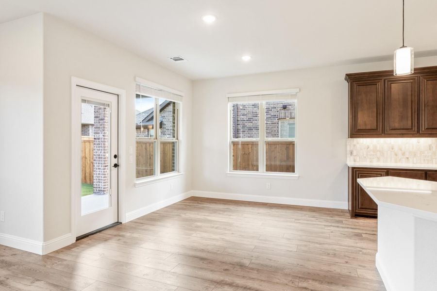 Open dining area with light wood floors, back door, and adjacent dark wood kitchen cabinets