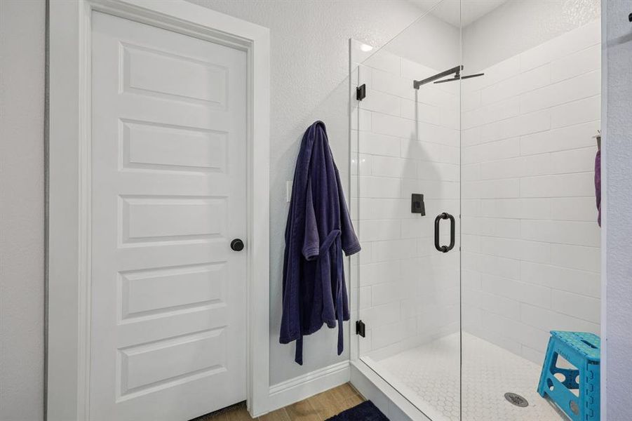 Bathroom featuring a shower stall, light wood-style floors, and a textured wall Bathroom featuring a shower stall, light wood-style floors, and a textured wall