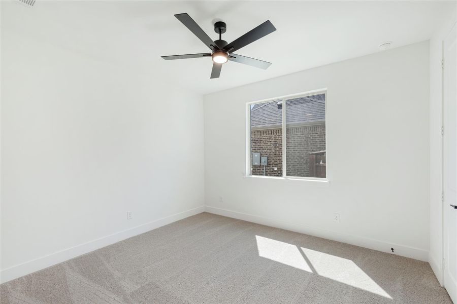 Empty bedroom with beige carpet, white walls, ceiling fan, and single window with natural light