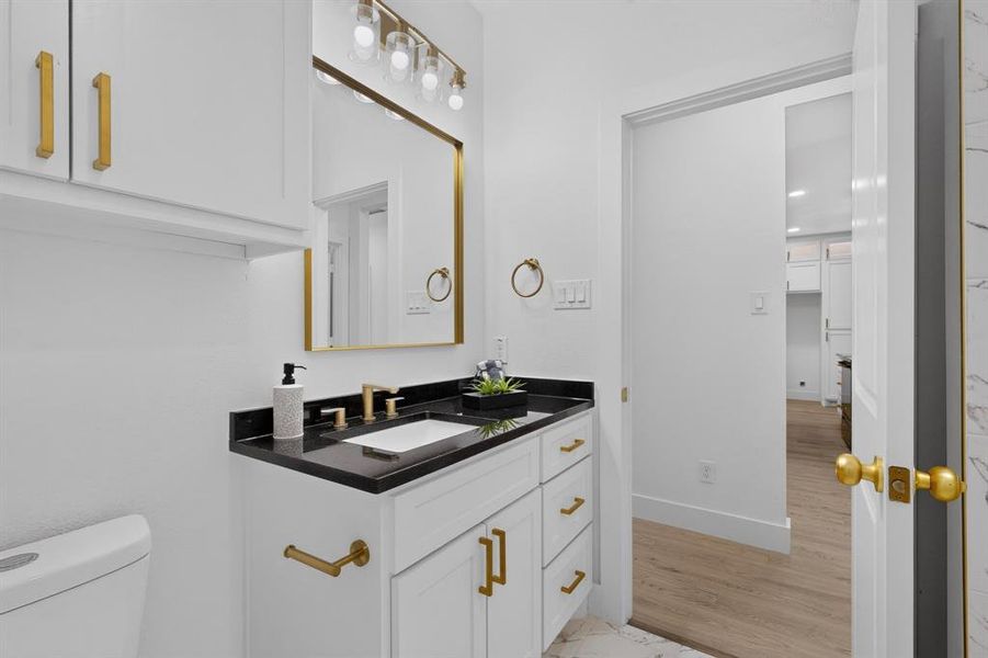Bathroom featuring a white vanity with gold-tone hardware, a black countertop, and an undermount sink