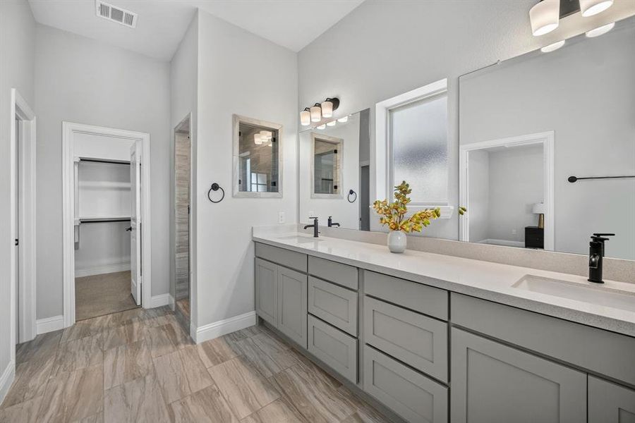 Double vanity with white countertops, matte black fixtures, light gray cabinetry, and walk-in shower.