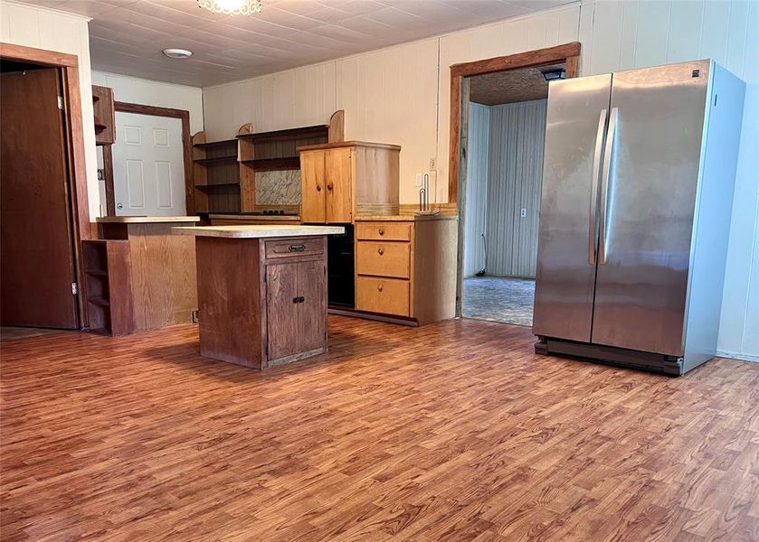 Kitchen featuring freestanding refrigerator, open shelves, wood finished floors, light countertops, and an island Kitchen featuring freestanding refrigerator, open shelves, wood finished floors, light countertops, and an island