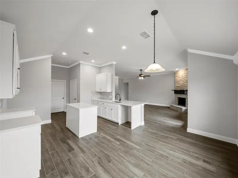 Kitchen featuring crown molding, open floor plan, ceiling fan, a fireplace, and visible vents