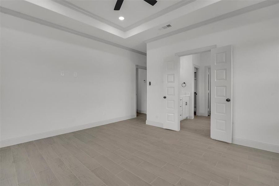 Unfurnished bedroom with light wood finished floors, ceiling fan, recessed lighting, and a raised ceiling Unfurnished bedroom with light wood finished floors, ceiling fan, recessed lighting, and a raised ceiling