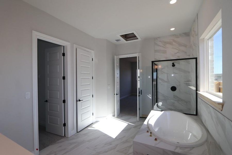 Indulge in this elegant primary bathroom featuring a freestanding tub, expansive walk-in shower, and luminous tile flooring.