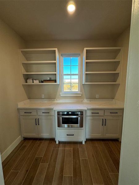 Kitchen with wall oven, light stone countertops, white cabinetry, and dark hardwood / wood-style floors