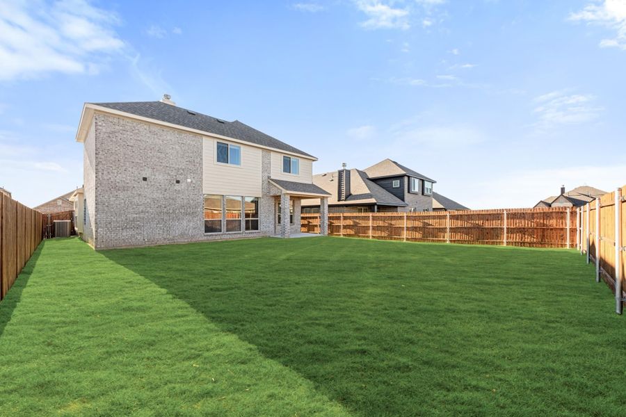Backyard of two-story brick home with large green lawn, covered patio, and wood privacy fence Backyard of two-story brick home with large green lawn, covered patio, and wood privacy fence