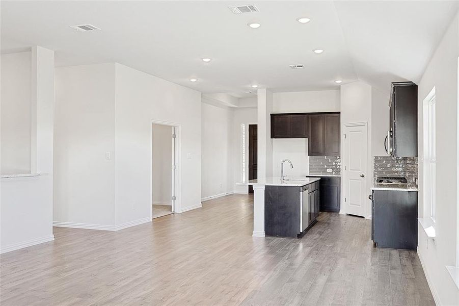 Kitchen featuring lofted ceiling, a center island with sink, sink, decorative backsplash, and light wood-type flooring