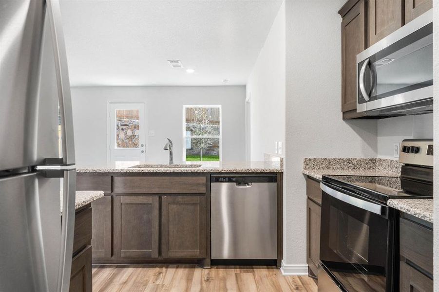 Kitchen with light stone counters, sink, dark brown cabinets, stainless steel appliances, and light wood-type flooring