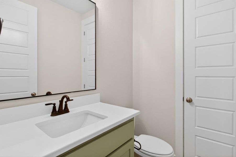 Bathroom featuring a white integrated sink, bronze-finish faucet, light green vanity cabinet, white countertop, and a framed mirror Bathroom featuring a white integrated sink, bronze-finish faucet, light green vanity cabinet, white countertop, and a framed mirror