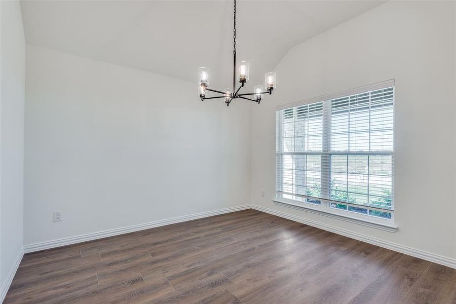 Spare room with dark hardwood / wood-style flooring, lofted ceiling, and a notable chandelier