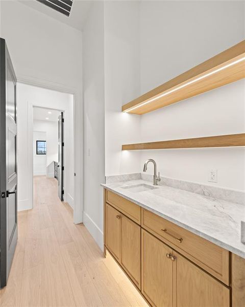 Bar area featuring open shelves, light stone countertops, light wood-style flooring, and light brown cabinetry