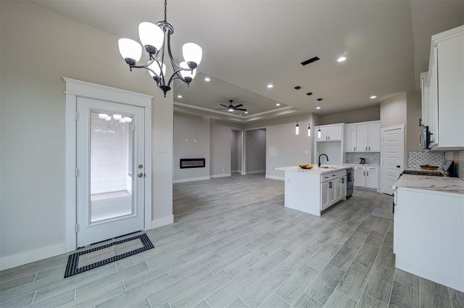 Kitchen with ceiling fan with notable chandelier, pendant lighting, tasteful backsplash, white cabinets, and a center island with sink