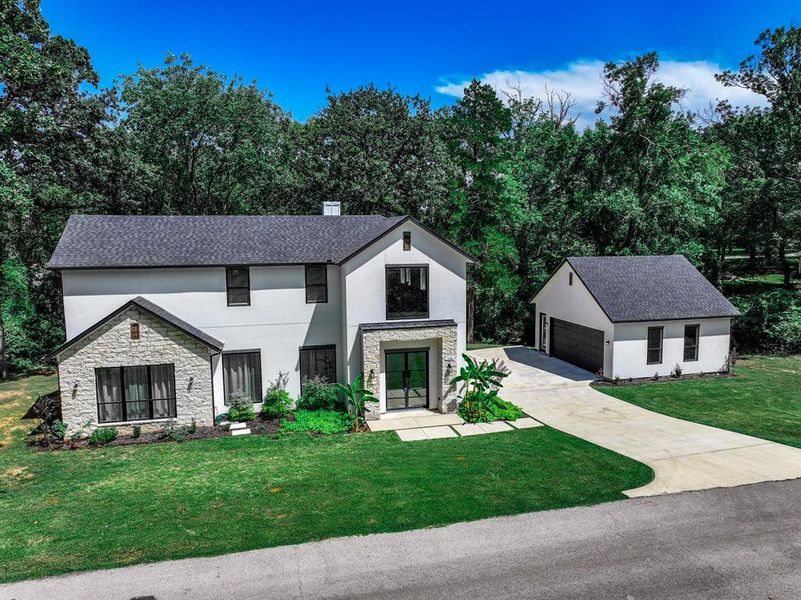 View of front of property with a detached garage, stucco siding, stone siding, and a front yard View of front of property with a detached garage, stucco siding, stone siding, and a front yard