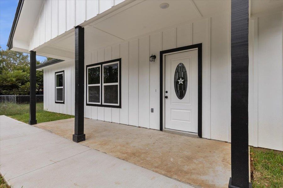 Board and batten siding meets stark black columns along this covered concrete front porch. Board and batten siding meets stark black columns along this covered concrete front porch.