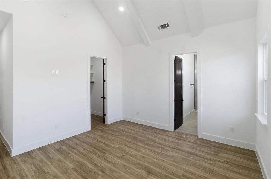 Unfurnished bedroom featuring a walk in closet, light wood-style floors, and lofted ceiling