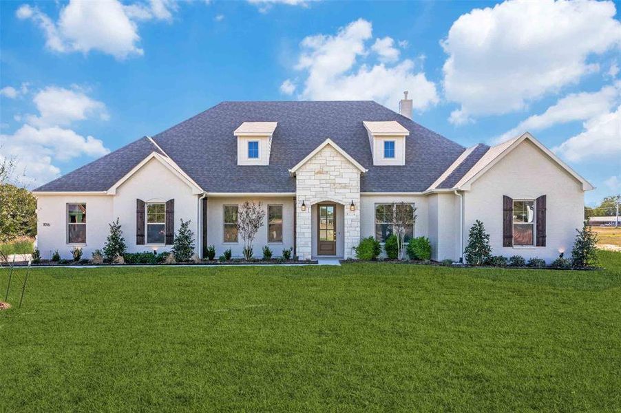 French country inspired facade with a shingled roof, a front yard, stone siding, and a chimney French country inspired facade with a shingled roof, a front yard, stone siding, and a chimney