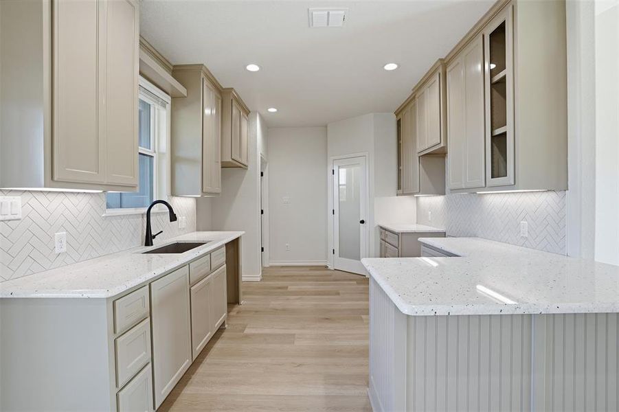 Kitchen featuring backsplash, light stone counters, light wood-style floors, a peninsula, and recessed lighting Kitchen featuring backsplash, light stone counters, light wood-style floors, a peninsula, and recessed lighting