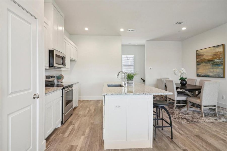 Kitchen featuring sink, appliances with stainless steel finishes, an island with sink, white cabinets, and light wood-type flooring