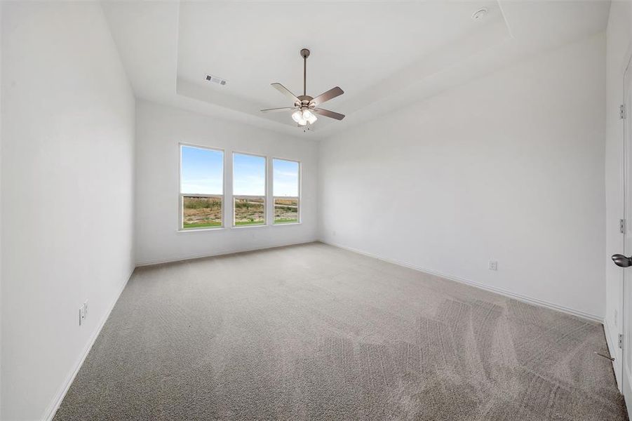 Empty room featuring a tray ceiling, light colored carpet, and ceiling fan Empty room featuring a tray ceiling, light colored carpet, and ceiling fan