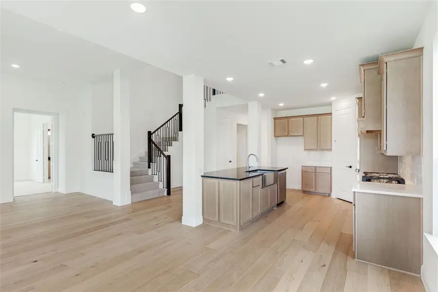 Open-concept kitchen with light wood cabinets, center island, and hardwood floors open to living area and staircase