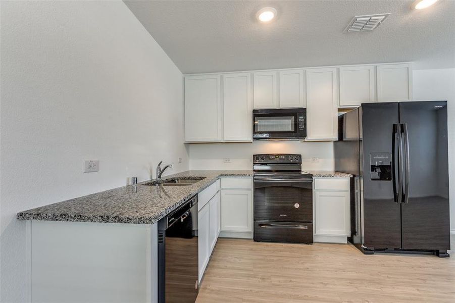 Kitchen featuring dark stone counters, black appliances, sink, light hardwood / wood-style flooring, and white cabinetry