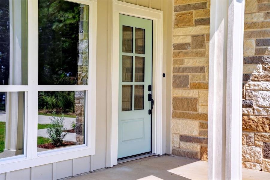 Entryway featuring a light blue paneled door with glass inserts, stone façade accents, a white column, and large windows with white trim