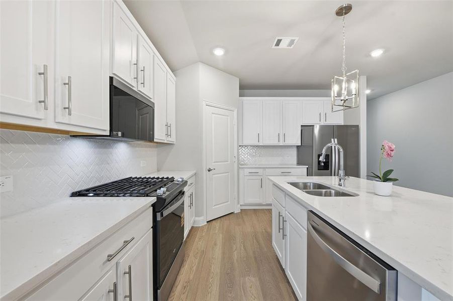 Kitchen featuring stainless steel appliances, hanging light fixtures, light wood-style floors, light stone counters, and recessed lighting