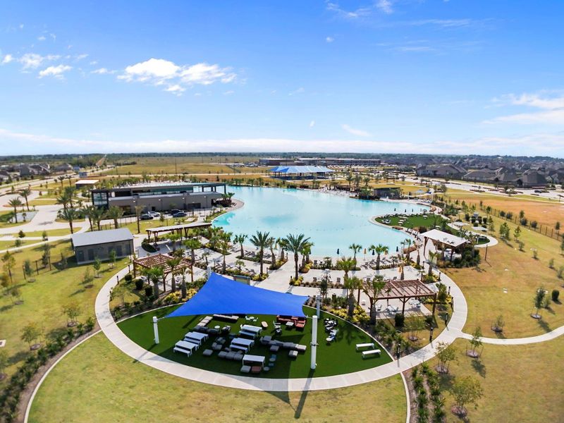 A breathtaking aerial view of The Sol Club Lagoon Amenity Village showcases Sunterra’s signature crystal-clear lagoon surrounded by white-sand beaches, lush green lawns, palm trees, and shaded pavilions. Enjoy resort-style living every day with scenic spaces designed for swimming, sunbathing, and relaxing with friends and family under the Texas sky!