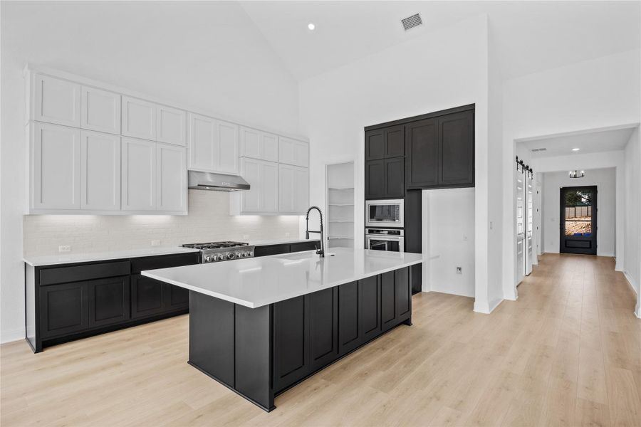 Kitchen with dual tone cabinets, light wood-style flooring, recessed lighting, a center island with sink, and stainless steel appliances