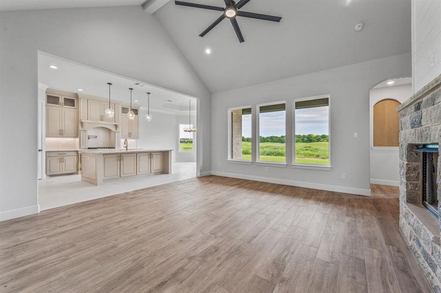 Unfurnished living room with ceiling fan, high vaulted ceiling, a stone fireplace, light wood-style flooring, and recessed lighting