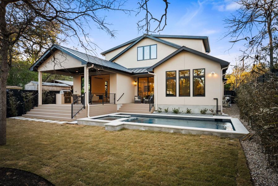 Back of house featuring area for grilling, a patio area, a standing seam roof, stucco siding, and a pool with connected hot tub