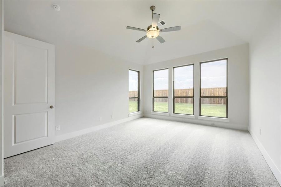 Spacious room featuring vaulted ceilings, a contemporary ceiling fan, and three large windows overlooking a private yard with a wood fence Spacious room featuring vaulted ceilings, a contemporary ceiling fan, and three large windows overlooking a private yard with a wood fence