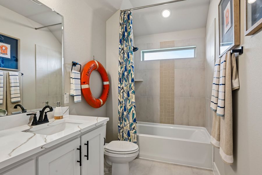Bathroom with white vanity, tiled tub-shower combo, and nautical decor including an orange life ring on the wall.