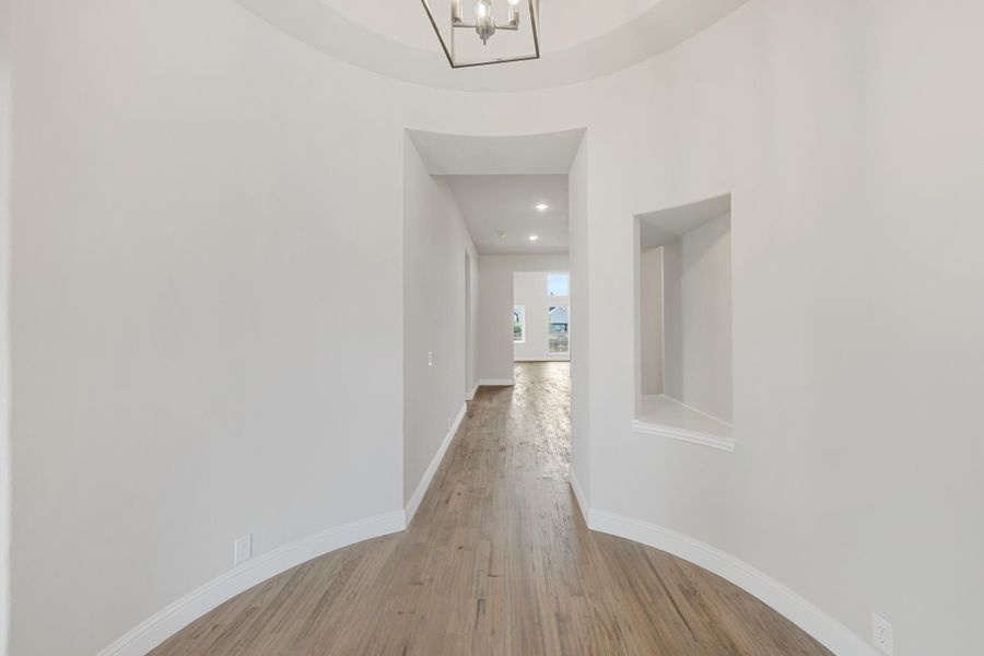 Curved entryway hallway with hardwood floors, chandelier, and wall niche leading to main living area Curved entryway hallway with hardwood floors, chandelier, and wall niche leading to main living area