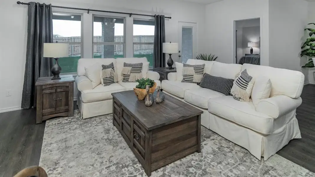 Spacious living area featuring wood-finish flooring, light-toned walls, and multiple windows with dark drapery