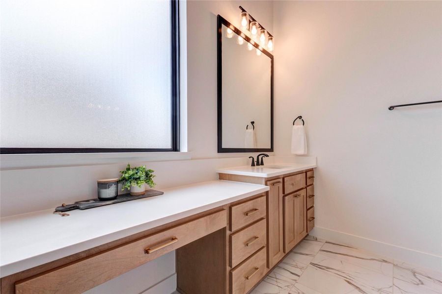 This photo features a modern bathroom vanity with a sleek countertop and black fixtures. It has ample storage with wooden cabinets and a large mirror. Adjacent is a spacious walk-in closet with wooden flooring. This photo features a modern bathroom vanity with a sleek countertop and black fixtures. It has ample storage with wooden cabinets and a large mirror. Adjacent is a spacious walk-in closet with wooden flooring.