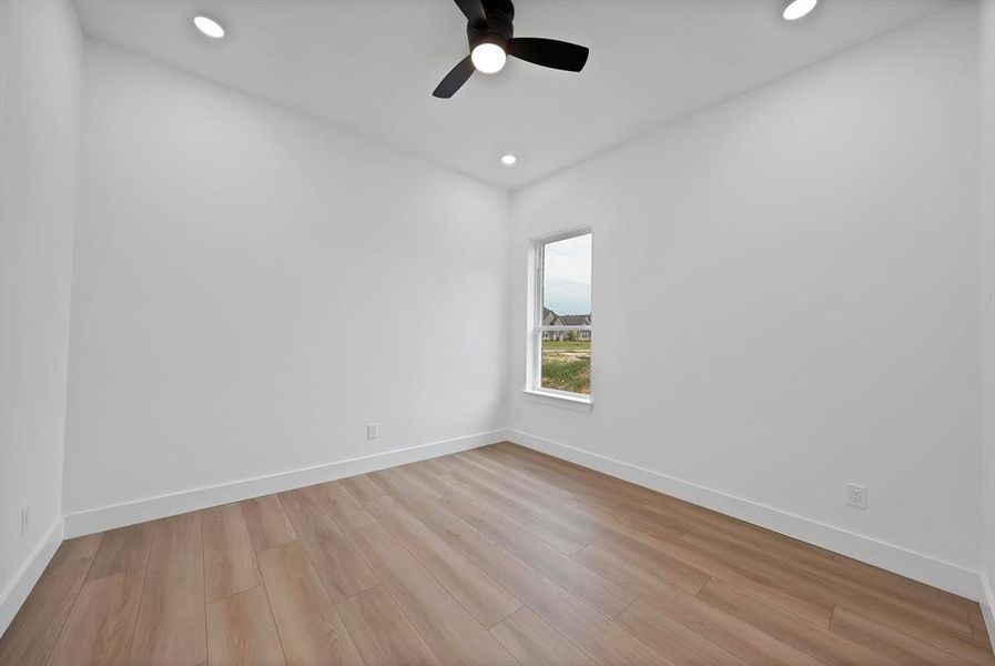 Spacious interior room featuring light wood-finish flooring, white baseboards, a white window frame, recessed lighting, and a black ceiling fan