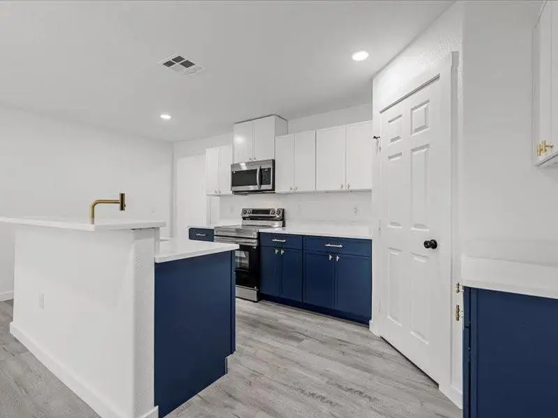 Kitchen featuring blue cabinets, white cabinetry, stainless steel appliances, light wood-style flooring, and recessed lighting