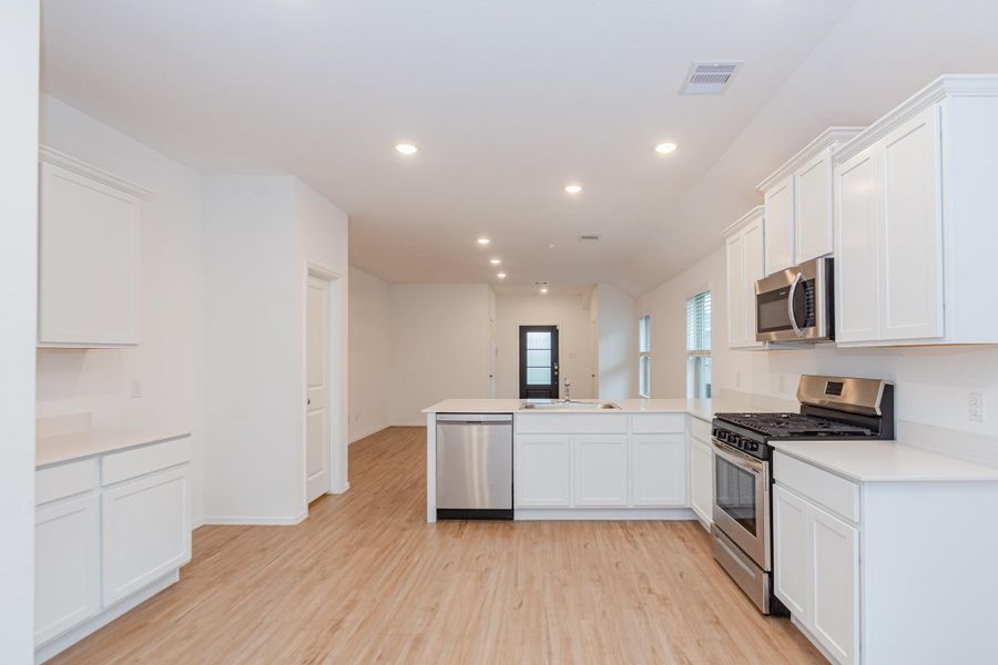 This modern kitchen features sleek white cabinetry, stainless steel appliances, and a spacious open layout with light wood flooring. Ideal for entertaining, it seamlessly connects to the living area, offering a bright and inviting atmosphere.