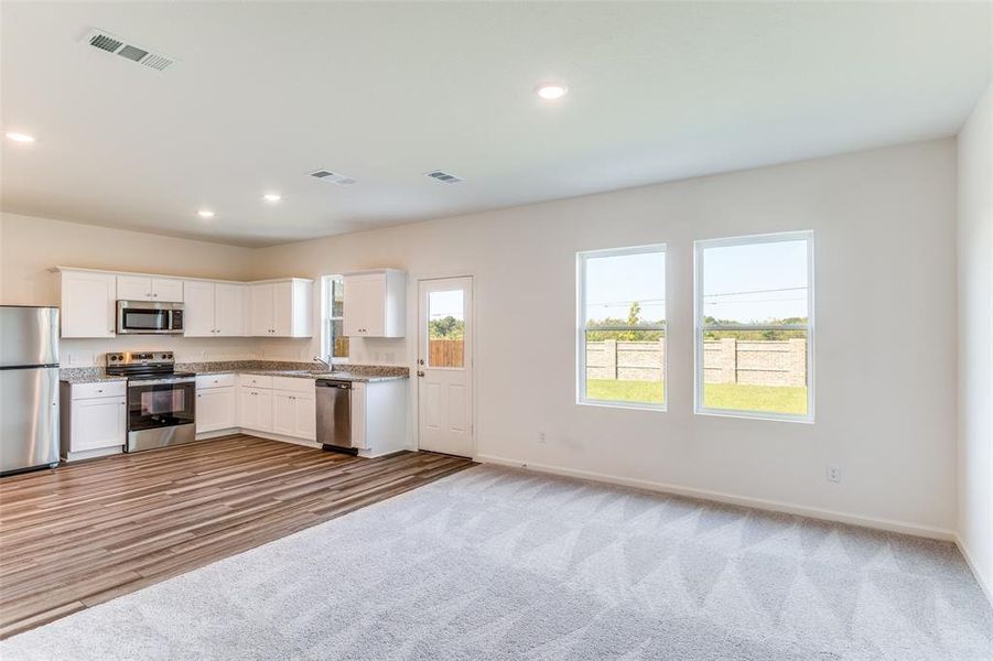 Kitchen with appliances with stainless steel finishes, white cabinets, recessed lighting, light carpet, and open floor plan
