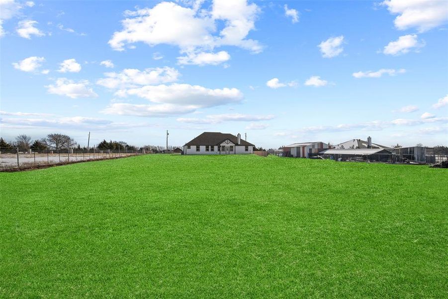 Expansive green lawn with a white single-story residence in the background featuring a dark shingled roof, multiple windows, and a chimney Expansive green lawn with a white single-story residence in the background featuring a dark shingled roof, multiple windows, and a chimney