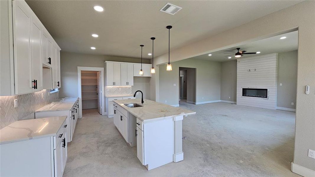 Kitchen with sink, ceiling fan, tasteful backsplash, and a kitchen island with sink