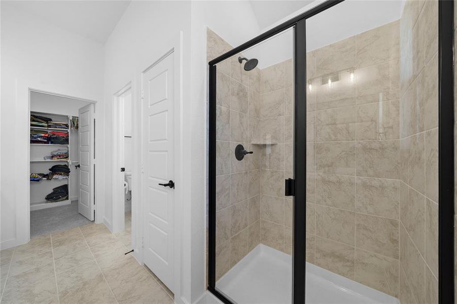 Walk-in shower with clear glass enclosure and matte black fixtures, complemented by a tiled interior and integrated shelf
